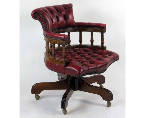 A reproduction captains style swivel chair, in red button down leatherette upholstery, on four swept legs terminating in cast