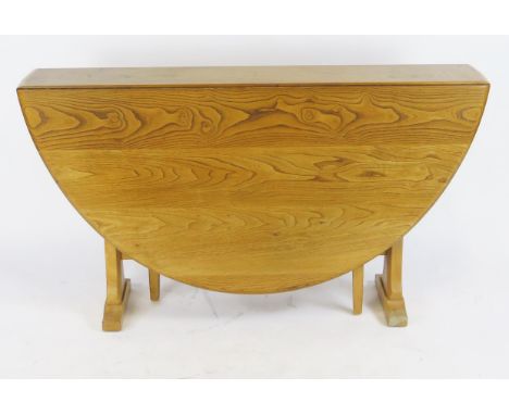 An Ercol Windsor elm and beech drop flap dining table, with gate-leg action, on trestle end supports, 140cm extended.