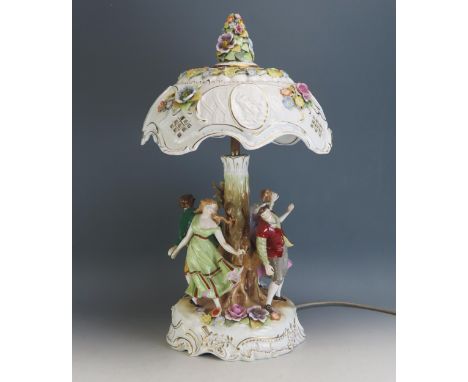 A continental porcelain figural table lamp and shade. with four figures dancing around a tree trunk, having a floral decorate