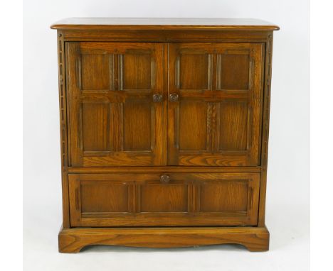 Ercol oak television cabinet of panelled construction with two panelled cupboard doors and single long drawer below, on brack