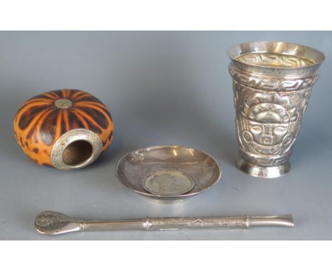 A South American silver tumbler, with embossed Aztec style decoration, 11cm high, a silver bombilla, silver dish with inset M