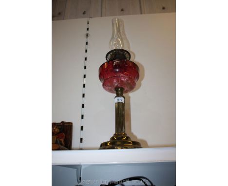 An oil lamp with reeded column base and cranberry glass reservoir.