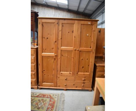 A modern pine triple wardrobe with part drawer base