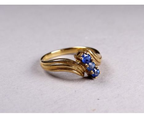 A 9ct yellow gold crossover ring - set with three sapphires, size N, weight 2.3g.