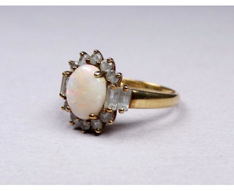 A 9ct yellow gold opal ring - the oval central stone surrounded by bright cut and baton cut clear stones, possibly topaz, siz