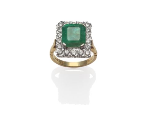 An Emerald and Diamond Cluster Ring, an emerald-cut emerald in a white claw setting, within a border of round brilliant cut d