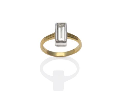 An 18 Carat Gold Diamond Solitaire Ring, the baguette cut diamond in a white rubbed over setting, to a yellow grooved shoulde