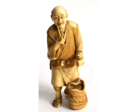 A Japanese Ivory Okimono, Meiji period (1868-1912), in the form of an old man smoking a pipe, a basket at his feet, holding a