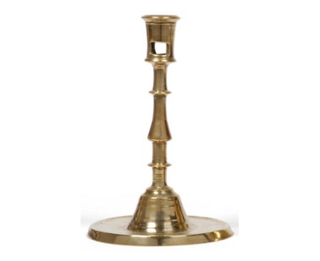 A 16th Century Dutch Brass Candlestick, the shallow circular base with a depressed drip tray rising to an inverted teardrop a