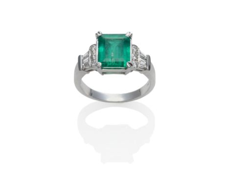 An 18 Carat White Gold Emerald and Diamond Ring, an emerald-cut emerald in a white claw setting, to shoulders each set with t