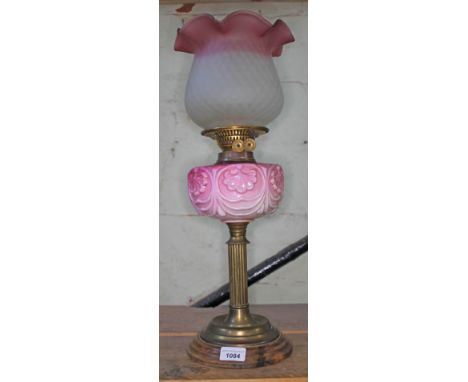 An oil lamp on brass support with wooden base, pink oil reservoir bearing leaf pattern, two coloured bowl (opaque, with pink 