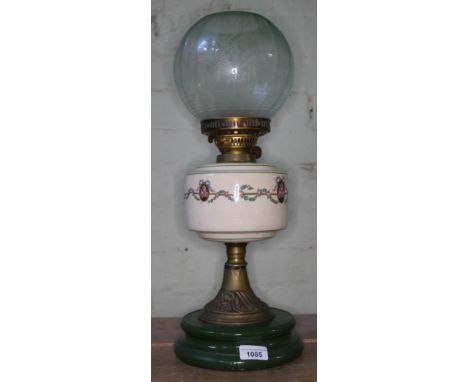 An oil lamp on green ceramic base, supported on brass column, with cream reservoir bearing floral pattern around middle. The 