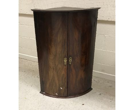 A George III mahogany bow fronted hanging corner cupboard, the two figured doors enclosing three shaped shelves, 77 cm wide x