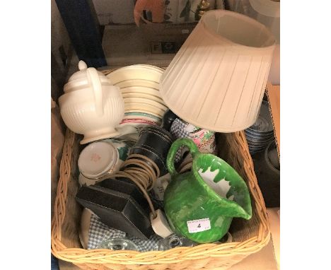 A wicker basket containing various modern china wares and a table lamp