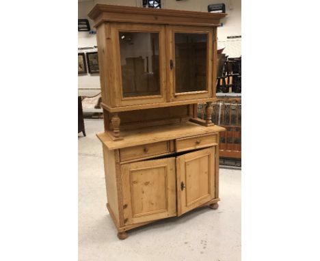 A Continental pine buffet, the glazed two door upper section enclosing two shelves, raised on turned cup and cover supports, 