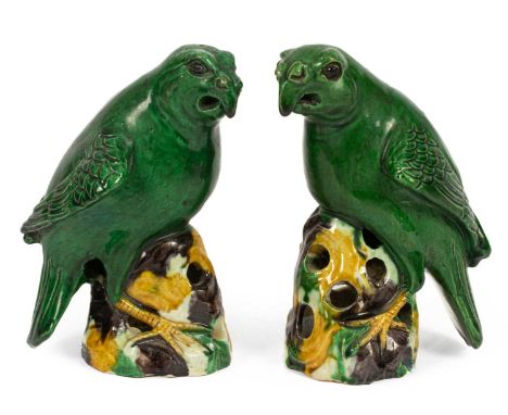 A pair of Chinese stoneware parrots, Kangxi style but likely later, in green, yellow and brown glaze, each modelled perched o