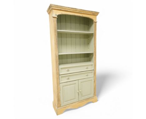Painted open bookcase over two long drawers and cupboard, with arched cornice above two shelves, in a distressed yellow and s
