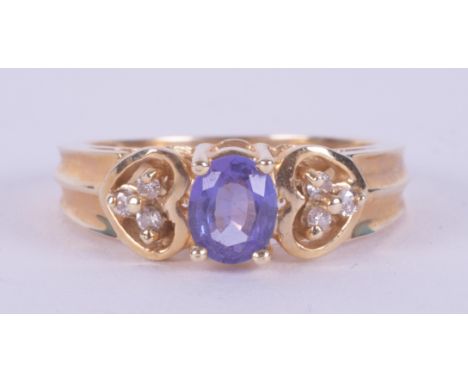 A 14k yellow gold ring set with a central oval cut tanzanite and a trefoil of diamonds to each side set in a heart shaped set