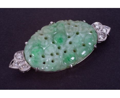 An 18ct white gold brooch set with a centre oval shaped piece of fancy carved jade, measuring approximately 3.5cm x 2.2cm, wi