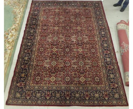 A modern machine made Persian style carpet, the red centre field with all over floral decoration in cream, mustard and blue w