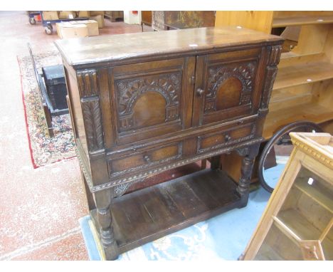 An oak carved press cupboard with twin arcaded doors above drawers on turned legs and lower shelf 115cm high, 105cm wide 