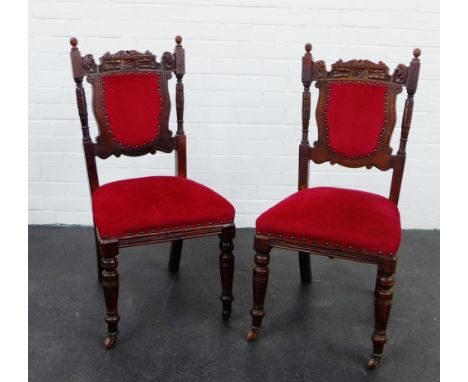 A pair of mahogany side chairs with carved top rails and red upholstered back and seats, on turned supports and ceramic casto