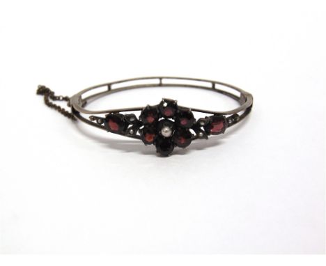 A GARNET AND SEED PEARL CLUSTER BANGLE circa 1900, internal diameter 5.8cm by 4.8cm