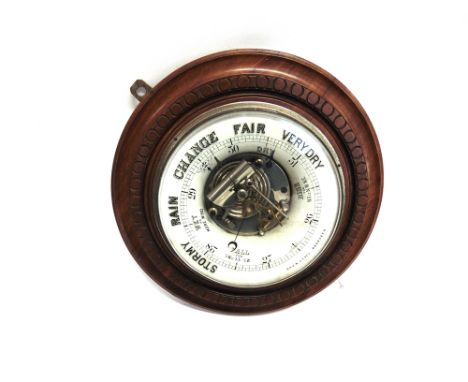 AN EDWARDIAN CARVED MAHOGANY FRAMED ANEROID BAROMETER  with visible mechanism within a ceramic frame inscribed 'HAY & LYALL, 