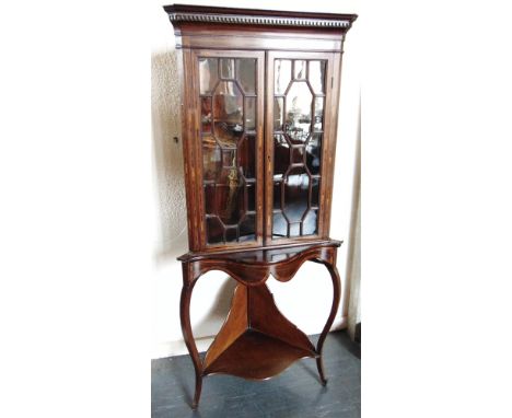 AN EDWARDIAN MAHOGANY CORNER CABINET with crossbanded decoration, dentil frieze above astragal glazed doors, the base with ca