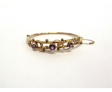 AN EDWARDIAN AMETHYST AND SEED PEARL BANGLE  stamped '15' to the catch, the three graduated round outs with seed pearl leaf m