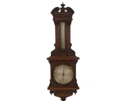 A late Victorian oak aneroid wheel barometer by Maple &amp; Co, of architectural form, having an urn and scroll pediment, car