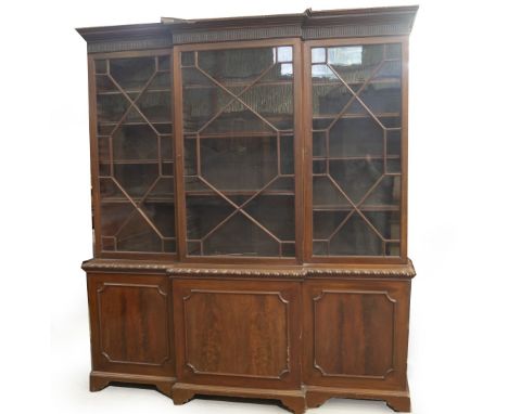 A mahogany breakfront cabinet bookcase in the Chippendale manner, the dentil moulded cornice having scoop carved frieze, over