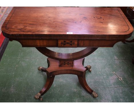 A Regency mahogany card table, hinged top enclosing a baize lined playing surface, bow shaped support, sabre legs, brass lion