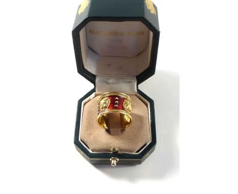 A yellow gold 'Lion Mask' ring by Elizabeth Gage, decorated with four masks on a red guilloche enamelled ground within a bead