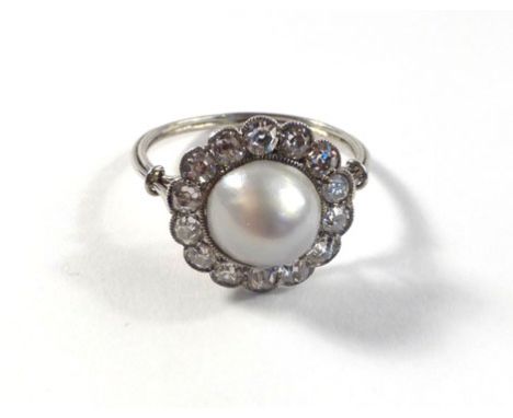 A French white gold ring set round pearl bordered by fourteen diamonds within a millegrain setting, estimated total diamond w