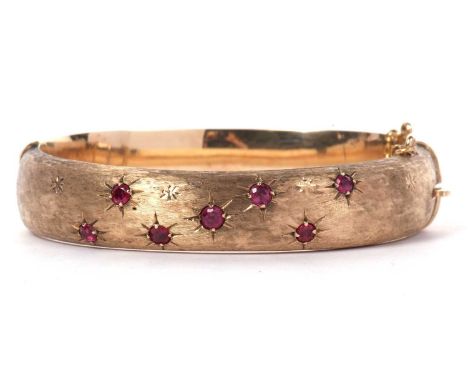 9ct gold and ruby set hinged bracelet, the top section a burnished design set with seven round cut rubies each in starburst e