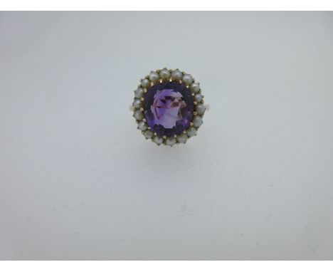 the oval cut amethyst in a border of 2mm seed pearls, plain tapered shank stamped '9ct', size N, length of cluster 1.6cm