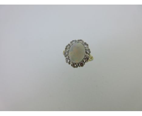 the oval cabochon opal above a border of ten round brilliant cut diamonds, fleur-de-lys shoulders and plain shank, size N, wh