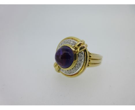 the round cabochon amethyst collet set in a ring of round brilliant cut diamonds which is crossed diagonally by a reeded bar,