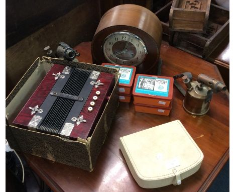Two brass blowlamps, jigsaw puzzles, a mantle clock and a squeeze box.