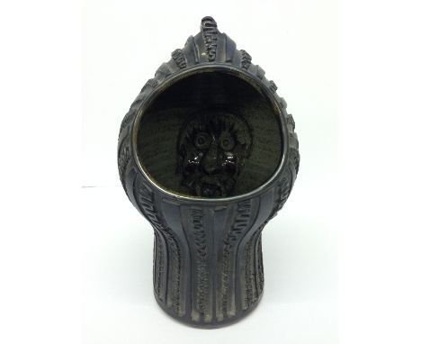 A Guy Sydenham Atlantis period carved matt black helmet lamp with internal green glazed male face with red cheeks decoration 