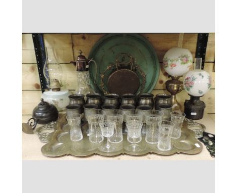 A shelf of items to include a brass gong, pewter goblets, oil lamps, trays and etched drinking glasses