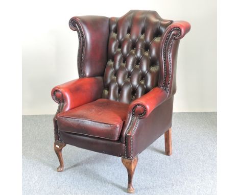A red leather wing back armchair, with a button back 