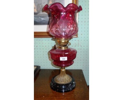 A Victorian oil lamp, having cranberry glass shade and reservoir on a pressed brass column and stepped circular ceramic eboni