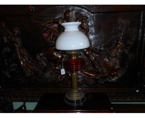 An Edwardian paraffin lamp, having an associated opaque glass shade, ruby glass reservoir on a brass column and foot with bla