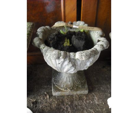 A reconstituted stone garden planter of leaf moulded form, having a petal cast foot on square plinth, 48cm diameter.