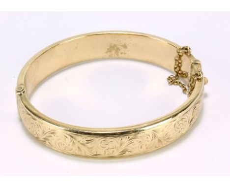 A 9ct yellow gold hollow snap bangle with engraved foliate scroll motifs, with safety chain, aperture 6 x 5.5cm, hallmarked f