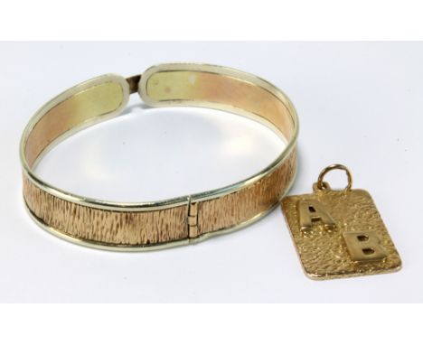 A yellow metal textured snap bangle, aperture 6.5 x 5.5cm (clasp af), and a 9ct gold rectangular pendant with applied initial