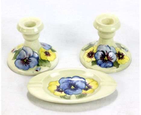 MOORCROFT; a pair of 'Pansy' pattern tubeline decorated squat candlesticks on pale green ground, impressed marks to base, hei