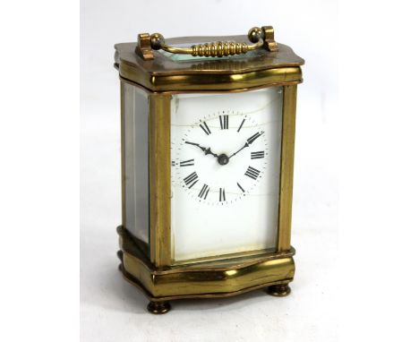 A circa 1900 brass carriage clock with serpentine sides, on turned brass supports, the rectangular enamelled dial with circul